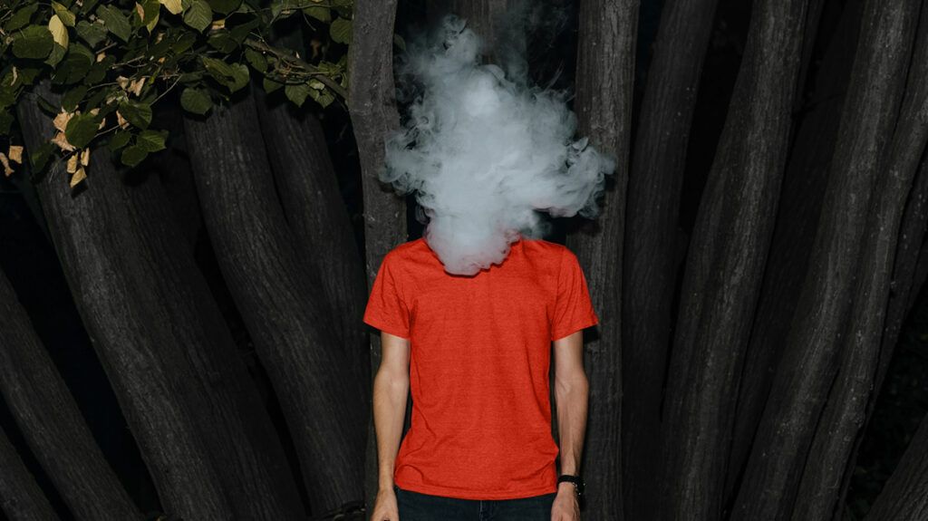 A man stands upright as his face is covered in what looks like cigarette or vape smoke